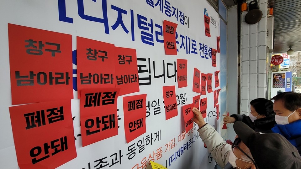 월계동 주민들이 '창구 남아라' 등 문구가 적힌 스티커를 은행 앞에 붙이고 있다[사진=연합뉴스]