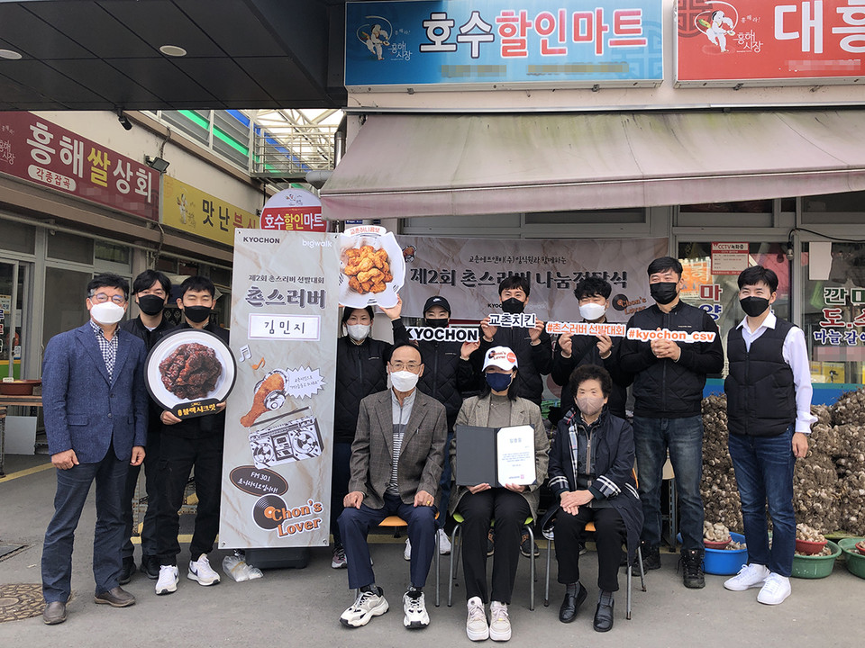 지난 21일 경북 포항 흥해읍에 위치한 호수할인마트에서 진행된 ‘제2회 촌스러버 선발대회’ 치킨 나눔 활동에서 교촌치킨 가맹점주 및 임직원들이 사연 당첨자와 함께 단체사진을 촬영하고 있다. [사진=교촌에프앤비]